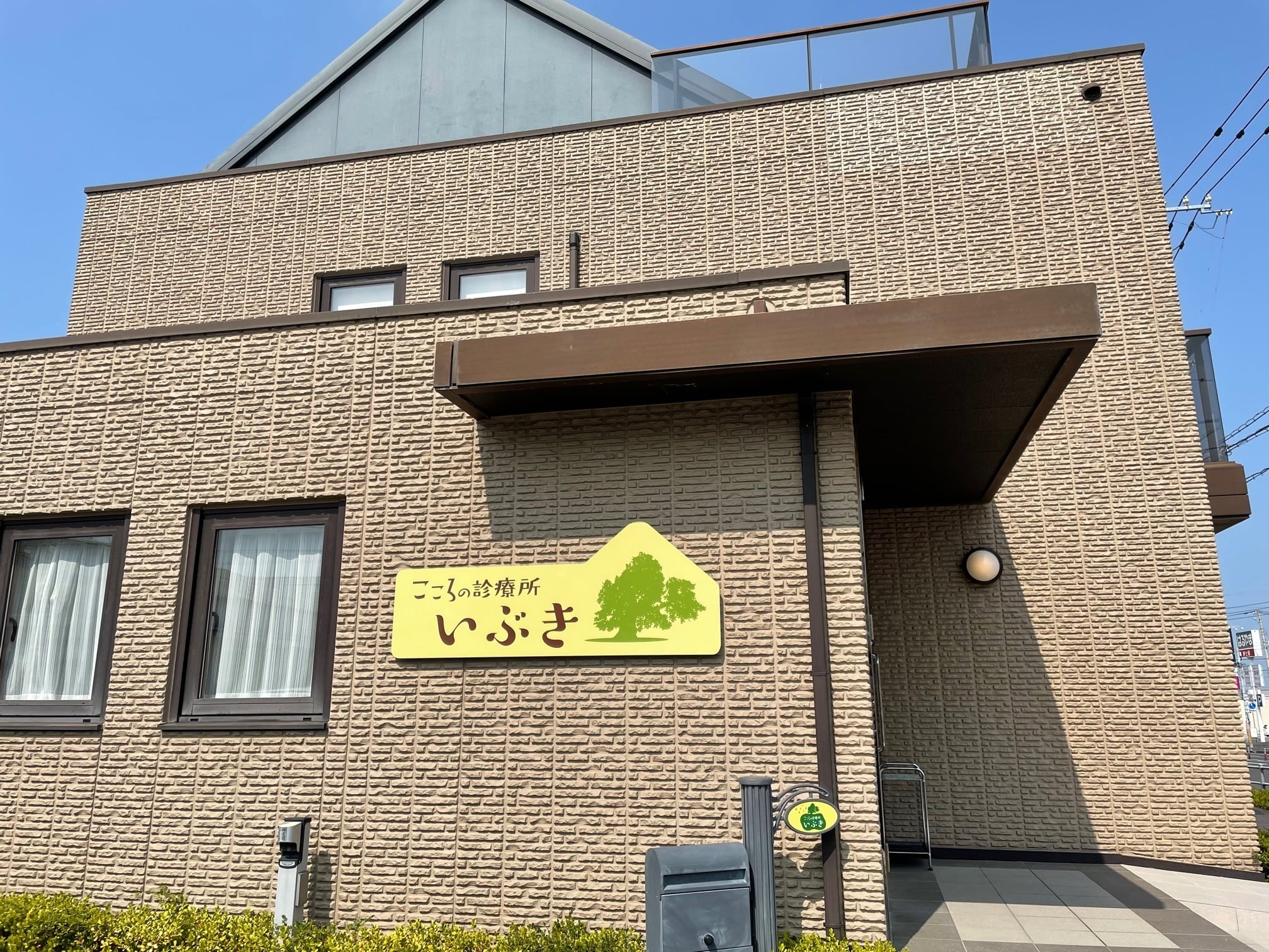 黄色い看板が目印のレンガ造りの介護施設建物外観。晴天下の施設全景。